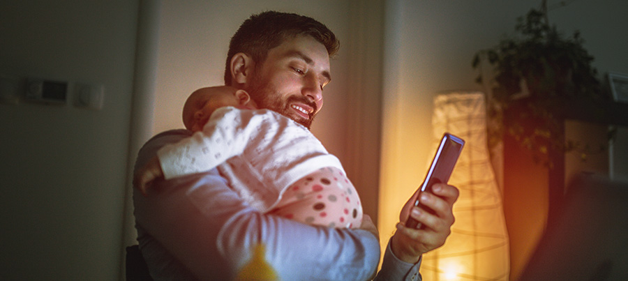 Vater mit Kind auf dem Arm schaut auf sein Smartphone.